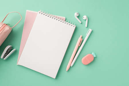 Back to school concept. Top view photo of stylish stationery notepads earbuds pens pencil-case mini stapler and pineapple shaped eraser on isolated pastel green background with copyspaceの写真素材