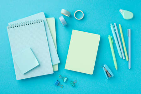 Back to school concept. Top view photo of stationery notepads blue adhesive tape binder clips colorful pens stapler paper sticky notes and round correction tape on isolated blue backgroundの写真素材