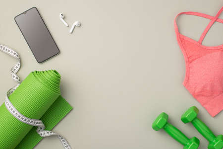 fitness concept. Top view photo of pink sports bra tape measure green exercise mat dumbbells earbuds...