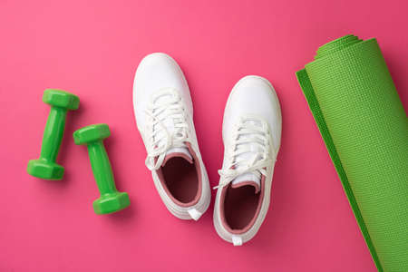 fitness concept. Top view photo of white sneakers green sports mat and dumbbells on isolated pink...