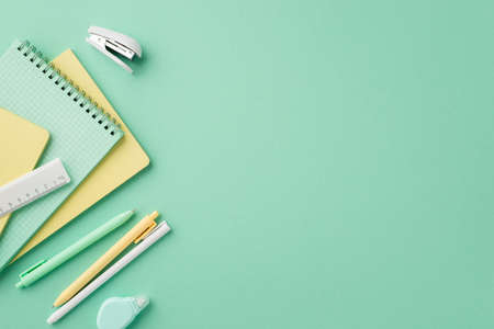 Back to school concept. Top view photo of stationery copybooks pens round correction tape ruler and mini stapler on isolated pastel green background with copyspaceの写真素材