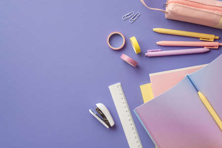 Back to school concept. Top view photo of stylish stationery open gradient color copybook pens pink pencil-case adhesive tape clips ruler and mini stapler on isolated violet background with copyspaceの写真素材