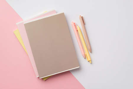 Back to school concept. Top view photo of school supplies stack of notebooks and pens on bicolor pink and white backgroundの写真素材