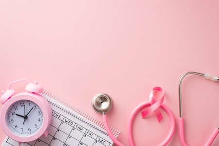 breast cancer awareness concept. Top view photo of stethoscope pink ribbon alarm clock and calendar on isolated pastel pink background with copyspaceの写真素材