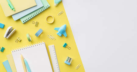 school accessories concept. Top view panoramic photo of colorful stationery plane shaped sharpener notepads ruler pens binder clips adhesive tape and stapler on bicolor yellow and white backgroundの写真素材
