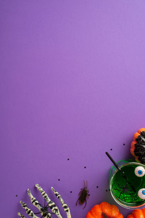 Halloween concept. Top view vertical photo of glass with green drink floating eyeball punch straw spiders pumpkins skeleton hand cockroach and confetti on isolated purple background with copyspaceの写真素材