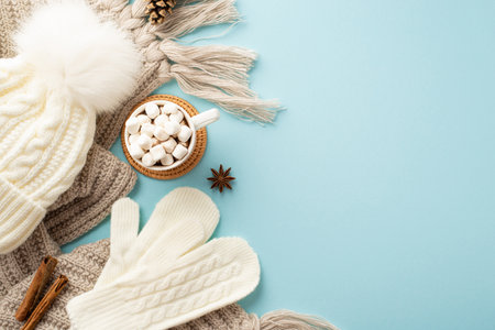 Top view photo of white mittens bobble hat knitted plaid mug of hot chocolate with marshmallow on rattan placemat pine cone anise cinnamon sticks on isolated pastel blue background with empty spaceの写真素材