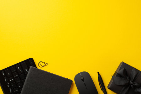 Black friday sale concept. Top view photo of black giftbox with ribbon bow notepad pen clip computer mouse and keyboard on isolated yellow background with empty spaceの写真素材