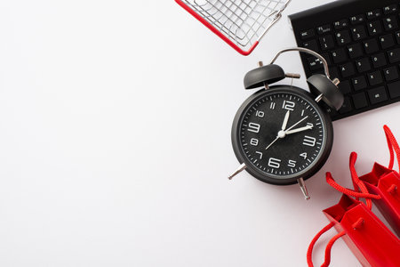 Cyber monday concept. Top view photo of alarm clock shopping cart keyboard and red paper bags on isolated white backgroundの写真素材