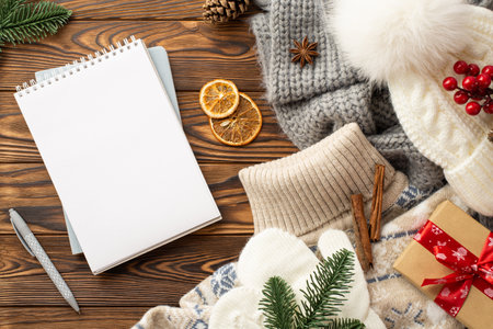 Top view photo of sweater headwear plaid mittens open reminder pen pine cone branches giftbox dried orange slices viburnum berries cinnamon sticks and anise on wooden desk background with empty spaceの写真素材