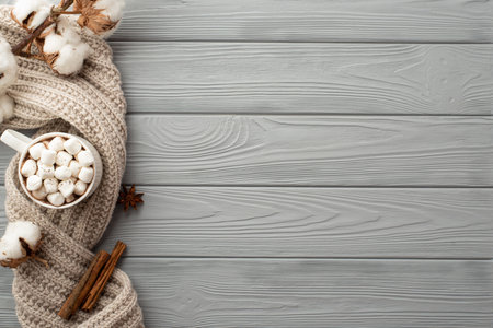 Winter atmosphere concept. Top view photo of mug of hot drinking with marshmallow cotton branch knitted scarf anise and cinnamon sticks on gray wooden desk background with copy spaceの写真素材