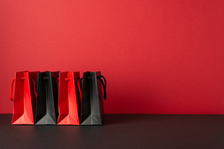 Black friday shopping concept. Photo of red and black paper bags on black tabletop red wall backgroundの写真素材