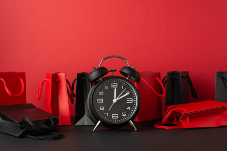 Black friday concept. Photo of alarm clock red and black paper bags on black table red wall backgroundの写真素材