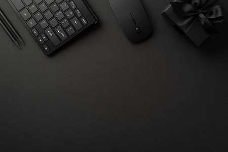 Black friday concept. Top view photo of black giftbox with ribbon bow pencils computer mouse and keyboard on isolated black background with empty spaceの写真素材