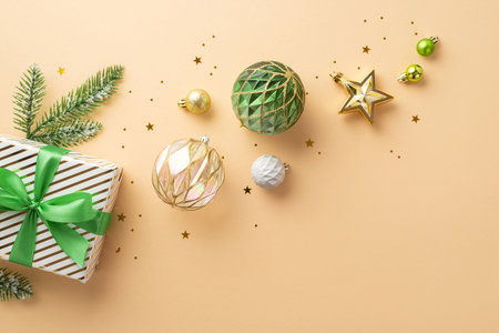 Christmas Eve concept. Top view photo of transparent white gold green baubles star ornament present box with bow pine branch in snow and confetti on isolated beige backgroundの写真素材