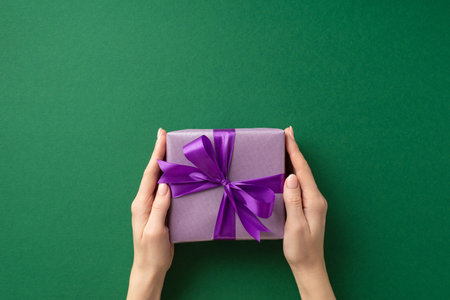 New year concept. First person top view photo of woman's hands giving violet giftbox with purple ribbon bow on isolated green background with blank spaceの写真素材