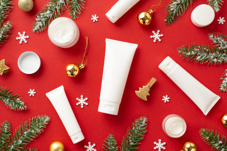 Winter season skincare concept. Top view photo of white tubes cream jars fir branches in hoarfrost golden baubles decorative clips and snowflakes on isolated red background with copyspaceの写真素材