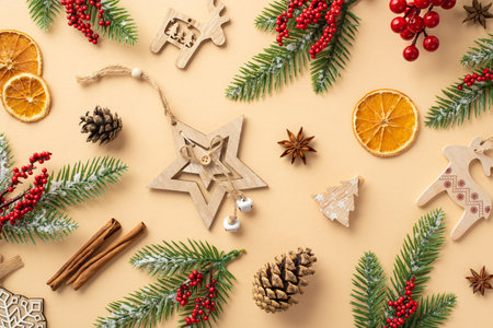 Christmas atmosphere concept. Top view photo of stylish wooden ornaments pine cones dried orange slices cinnamon sticks spruce branches in frost and mistletoe berries on isolated beige backgroundの写真素材