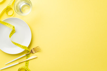 weight loss concept. Top view photo of plate glass of water measuring tape knife and fork on isolated pastel yellow background with empty spaceの写真素材