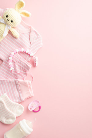 baby shower concept. Top view vertical photo of pink infant clothes shirt pants socks knitted bunny toy pacifier teether chain and milk bottle on isolated pastel pink background with copyspaceの写真素材