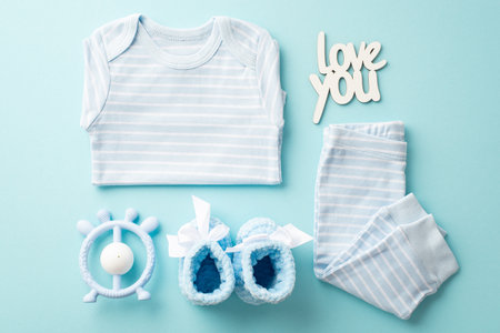 baby boy concept. Top view photo of blue shirt pants inscription love you knitted booties and teether on isolated pastel blue backgroundの写真素材