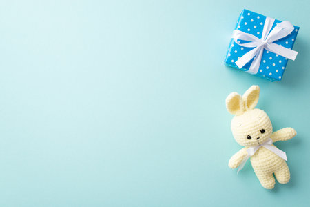 baby accessories concept. Top view photo of blue giftbox with ribbon bow and yellow knitted bunny toy on isolated pastel blue background with copyspaceの写真素材