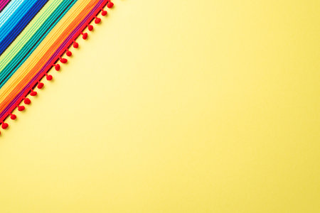 Above top view photo of textile striped colorful mexican poncho on light yellow background with...