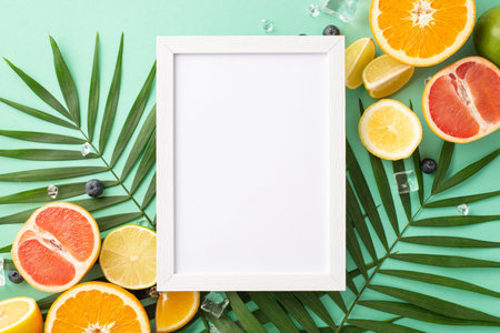 Citrus blast concept. Top view of fresh oranges, lemons, limes and grapefruits with palm leaves on turquoise background with empty frame for advert or logoの写真素材