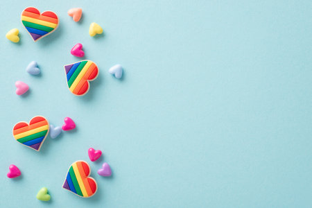 Symbolic LGBTQ+ accessories like rainbow-colored heart pins seen from above on a pastel blue background, with plenty of space for text or advertの写真素材