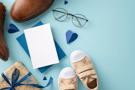 Dad receives sweet Father's Day gifts from son. Top view shot of dad's leather shoes, baby boy's sneakers, hearts, envelope with postcard, and giftbox on pastel blue background with space for textの写真素材