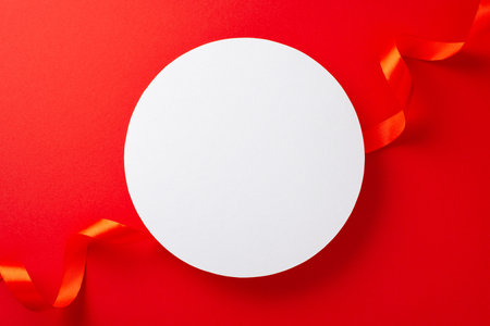 Top view photo of white empty circle surrounded by bright red ribbon and paper origami hearts on isolated red background with copy-spaceの写真素材