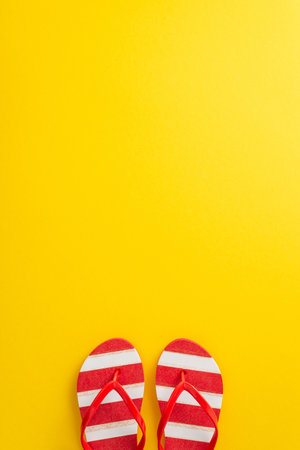Celebrate the spirit of summer with this captivating top vertical view minimal flat lay. Featuring a pair of red striped flip-flops on a vibrant yellow backdrop, with an empty space for text or advertの写真素材