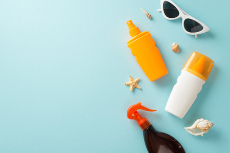 sun protection collection. Blank space for branding on a pastel blue background featuring top view of sunblock oil and SPF cream bottles without labels, sunglasses, shells, and starfishの写真素材