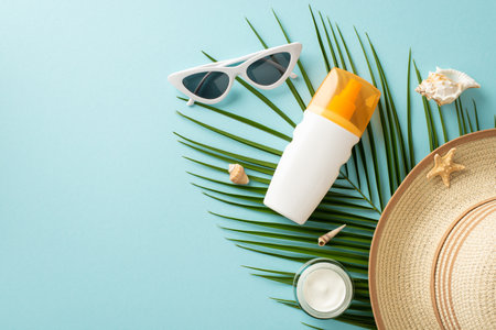 Safe beach sunbathing concept. Above view photo of palm leaf with sunscreen spray and cream, shells, sunglasses with straw hat on it on light blue isolated background with copy-spaceの写真素材