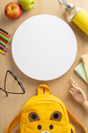 Play group concept. Vertical top view of crayons, copybooks, glasses, mannequin hand, backpack in shape of cute animal, water bottle, apples on wooden table backdrop with circle for text or advertの写真素材