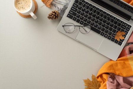 Top view image encapsulates the essence of working from home, showcasing a laptop with a cozy blanket, pinecones, spices, glasses and a cup of coffee on gray isolated backdrop with copyspace for textの写真素材