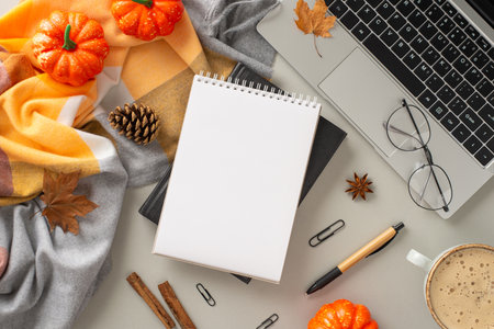 Coziness of working from home with laptop concept. Above view photo of notebook surrounded by blanket, pumpkins, pinecones and spices, office supplies, glasses and laptop on isolated gray backgroundの写真素材