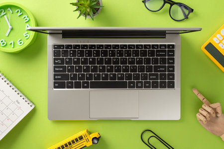 Engage in distant learning with this top-view shot, showcasing a laptop, calendar, clock, glasses and school supplies like calculator, paper clips on isolated light green backgroundの写真素材