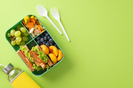 Wholesome snack arrangement for school. Top view featuring lunchbox with variety of fresh fruits,...