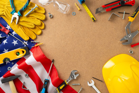 Labor day theme. Top view of American flag, screwdriver, wrench, hammer, pliers, screws, nuts, gloves, glasses, dowel nails, level and more on plywood backdrop. Perfect for promotions or discountsの写真素材