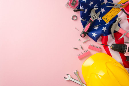 Commemorating female labor on American Labor Day. High-angle photo showcasing a pink backdrop with an American flag and building tools, providing copyspace for ads or text placementの写真素材