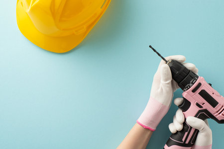 Tribute to hardworking women on Labor Day. Top view of woman's gloved hands with pink feminine drill...