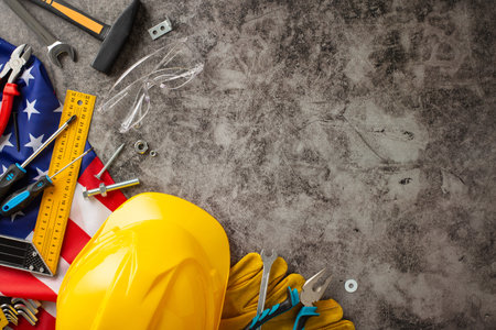 Recognizing the significant role of construction workers on American Labor Day. Above photo of flag, helmet, gloves and building tools on grunge textured gray concrete. Copyspace available for ads or textの写真素材