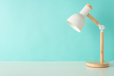 Inspirational study area. Side view photo of tabletop with beautiful desk lamp against pastel teal wall. Ample space for text or promotionの写真素材