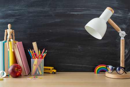 Get inspired by this school-oriented setup: side view photo of desk essentials, stationery, books, lamp, mannequin, glasses, apple and more against chalkboard backdrop, offering space for text or adsの写真素材