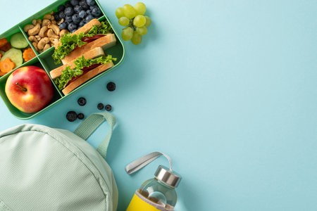 Wholesome school break scene captured from above, showcasing a lunchbox filled with sandwiches and snacks, blue rucksack and bottle set against a blue isolated backdrop with ample copyspaceの写真素材