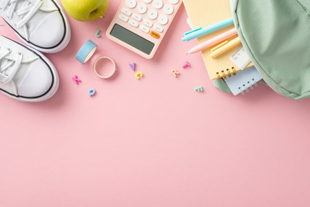 Fashionable educational gear arrangement.Top view of backpack with pens, ruler, adhesive tape, copybooks, alphabet letters, calculator, shoes, apple on soft pink backdrop, space for text or promotionの写真素材