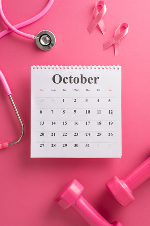 Advocating Breast Cancer Awareness Month. Bird's-eye top vertical view of a calendar, stethoscope, weights and pink ribbon on a bright pink isolated background, with copyspace for text or promotionsの写真素材