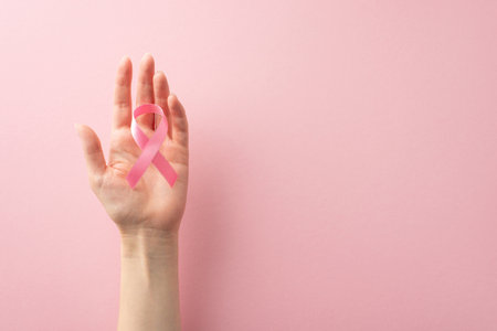 Raise your voice this International Breast Cancer Awareness Month. Top view photo of woman's hands holding a pink ribbon on pastel pink backdrop, offering copyspace for text or advertisingの写真素材