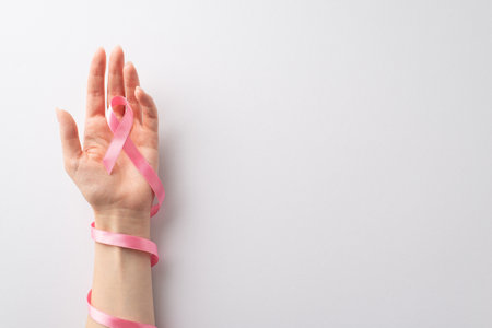 Illustrating International Breast Cancer Awareness Month. Top view of woman's hands holding pastel pink ribbon on a white isolated background. Perfect for promotional content or textの写真素材